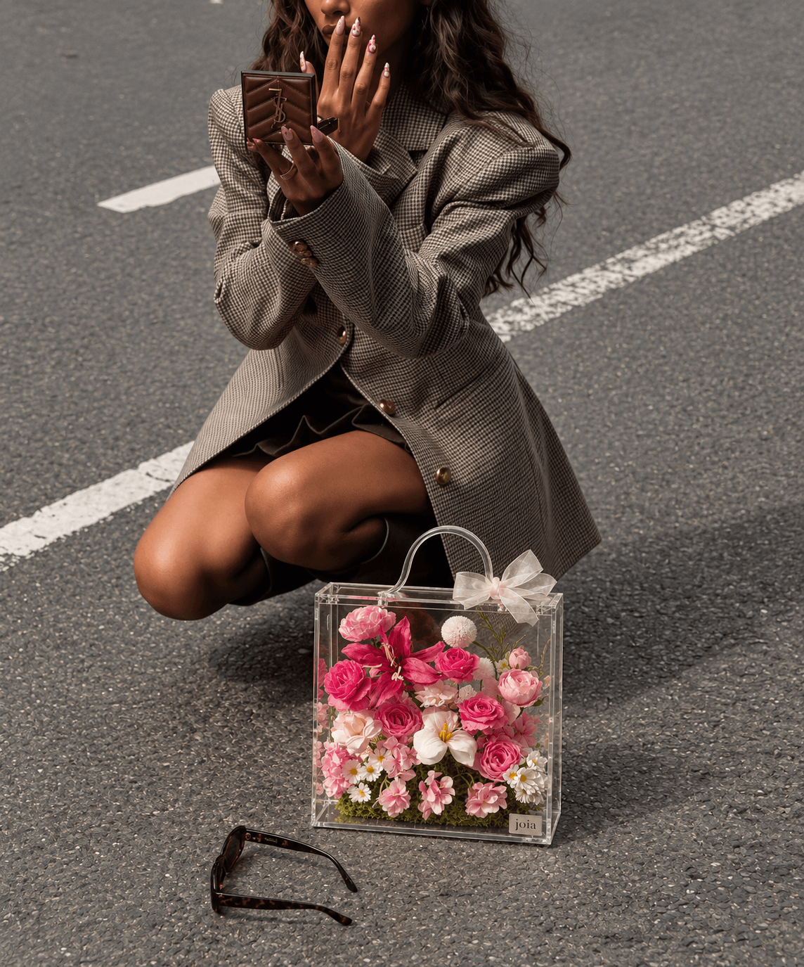 Woman applying lipstick beside a pink JOIA flower valise
