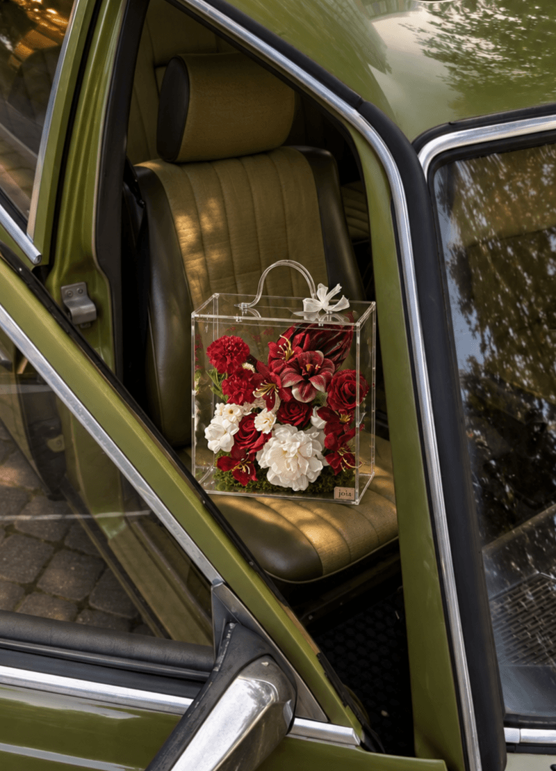 A red and ivory JOIA flower valise resting on the seat of a vintage green car